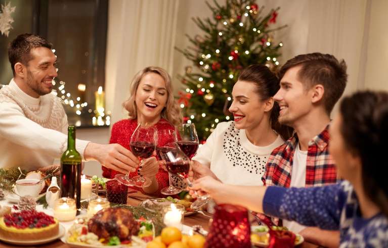 A group of friends gathered around a festive dinner table, toasting with glasses of red wine.