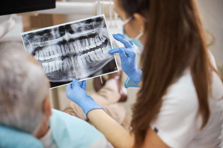 A female dentist wearing blue gloves and a white coat holds up a dental X-ray.